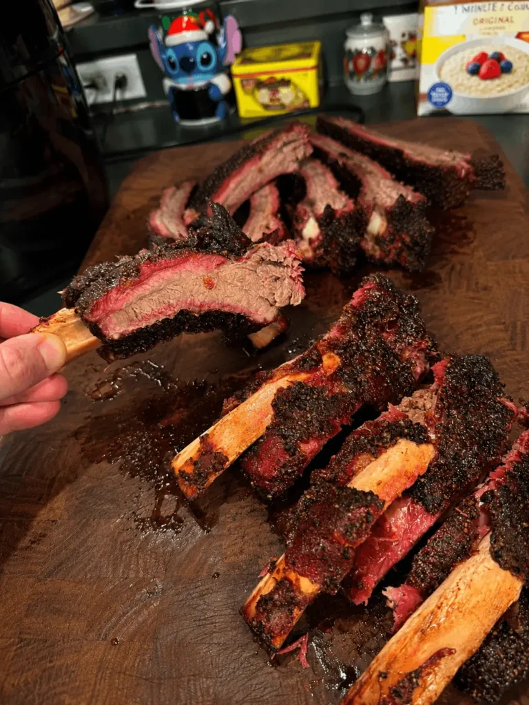 Hand holding a smoked beef back rib showing tender, pull-apart meat and smoke ring