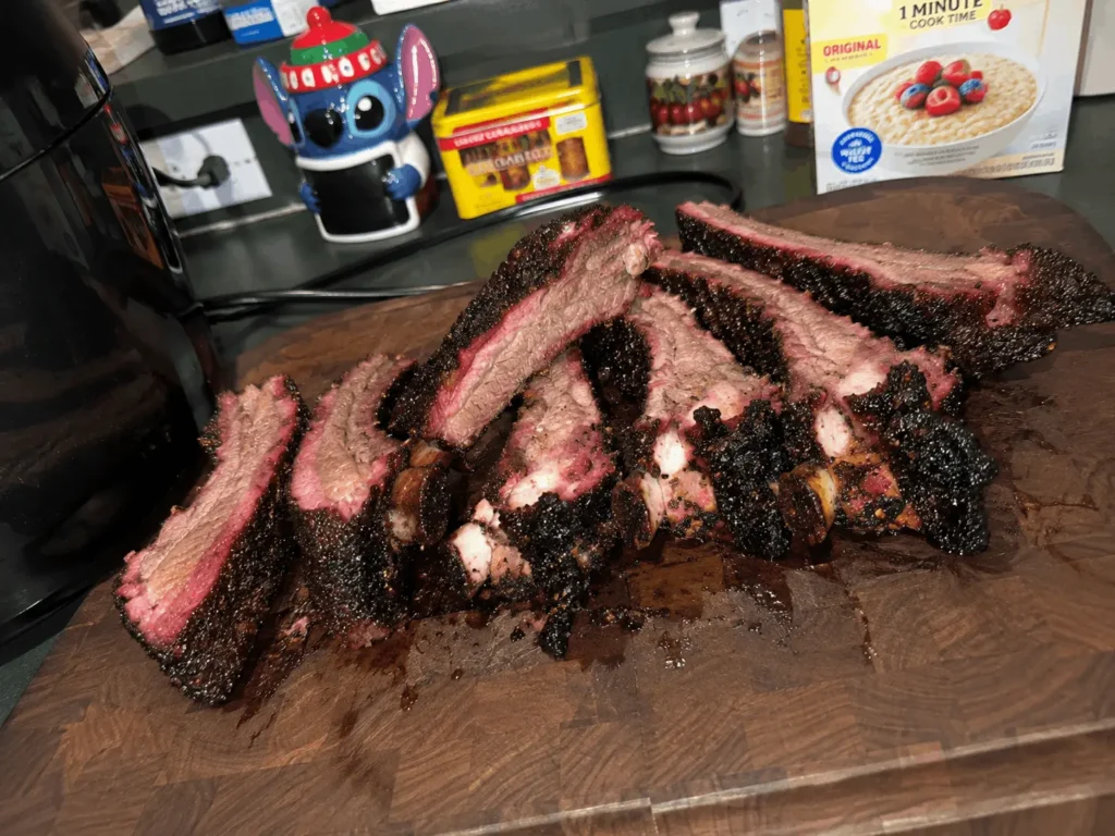 Sliced smoked beef back ribs with a dark peppery bark and pink smoke ring on a wood cutting board